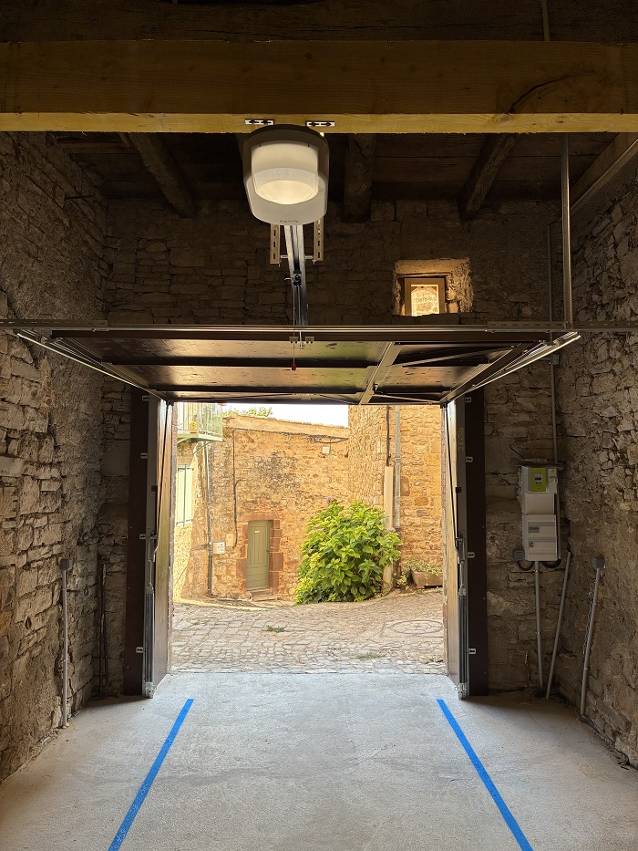 Portail relevé sous le plafond du garage, ouvrant sur une ruelle pavée de la vieille cité