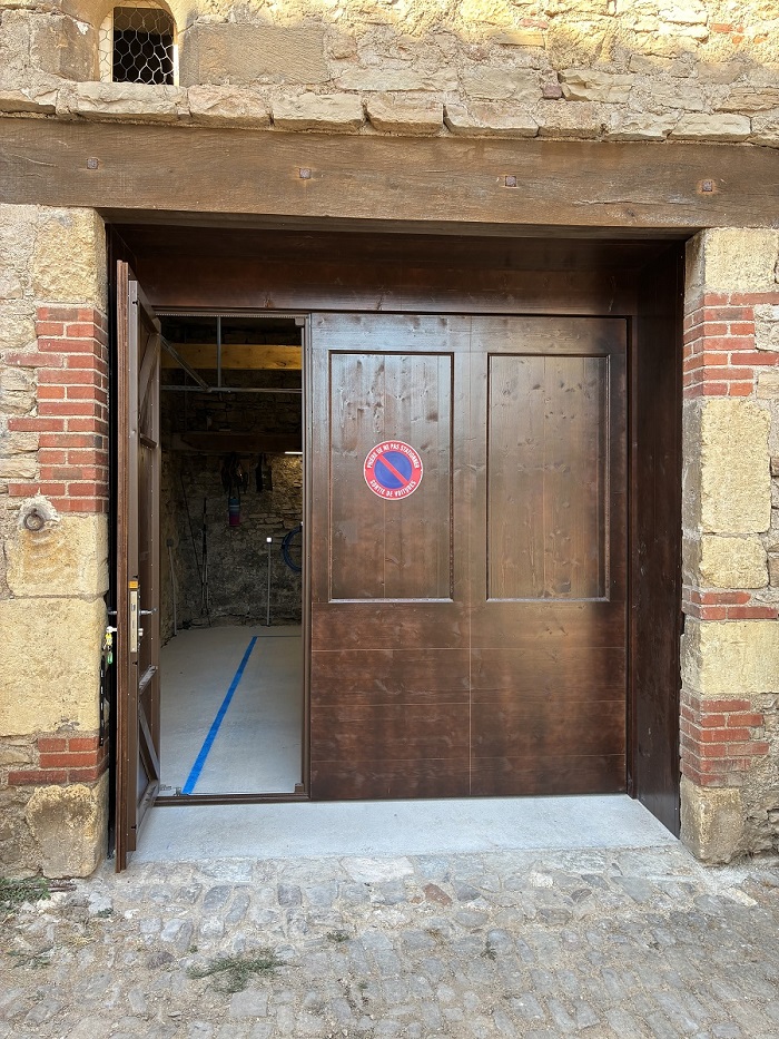 Portail de garage en bois fermé avec son portillon piéton ouvert sous un linteau en bois